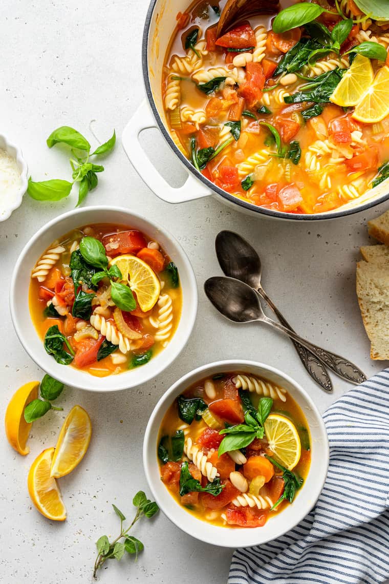 This hearty vegetable stew is packed with nutrients thanks to carrots, onion, and tomatoes, plus pasta and white beans for a satisfying meal. two bowls of vegetable and pasta stew with lemon and basil