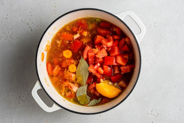 This hearty vegetable stew is packed with nutrients thanks to carrots, onion, and tomatoes, plus pasta and white beans for a satisfying meal. Overhead view of vegetable stew in pot after adding tomatoes, lemon, and bay leaves
