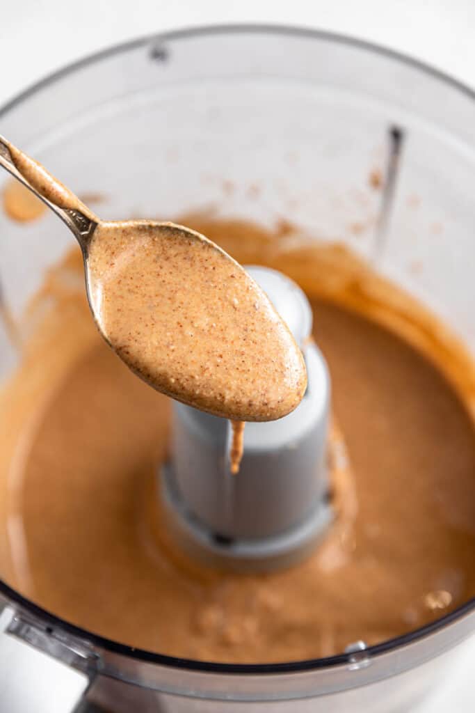 spoon holding almond butter over a food processor