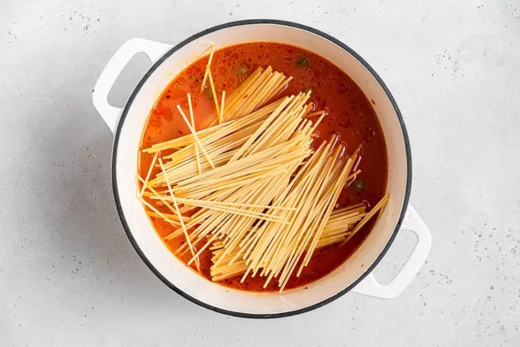 adding pasta to a pot with tomato sauce