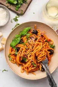 bowl of pasta puttanesca with olives and basil