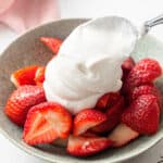 adding coconut whipped cream to strawberries