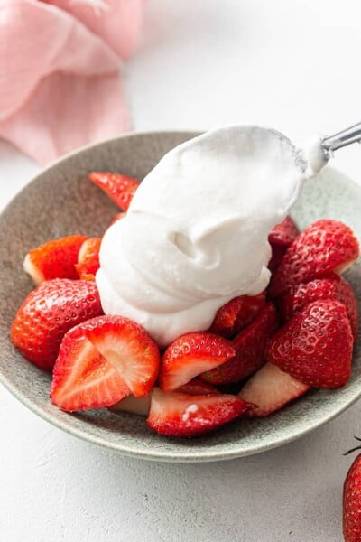 adding coconut whipped cream to strawberries