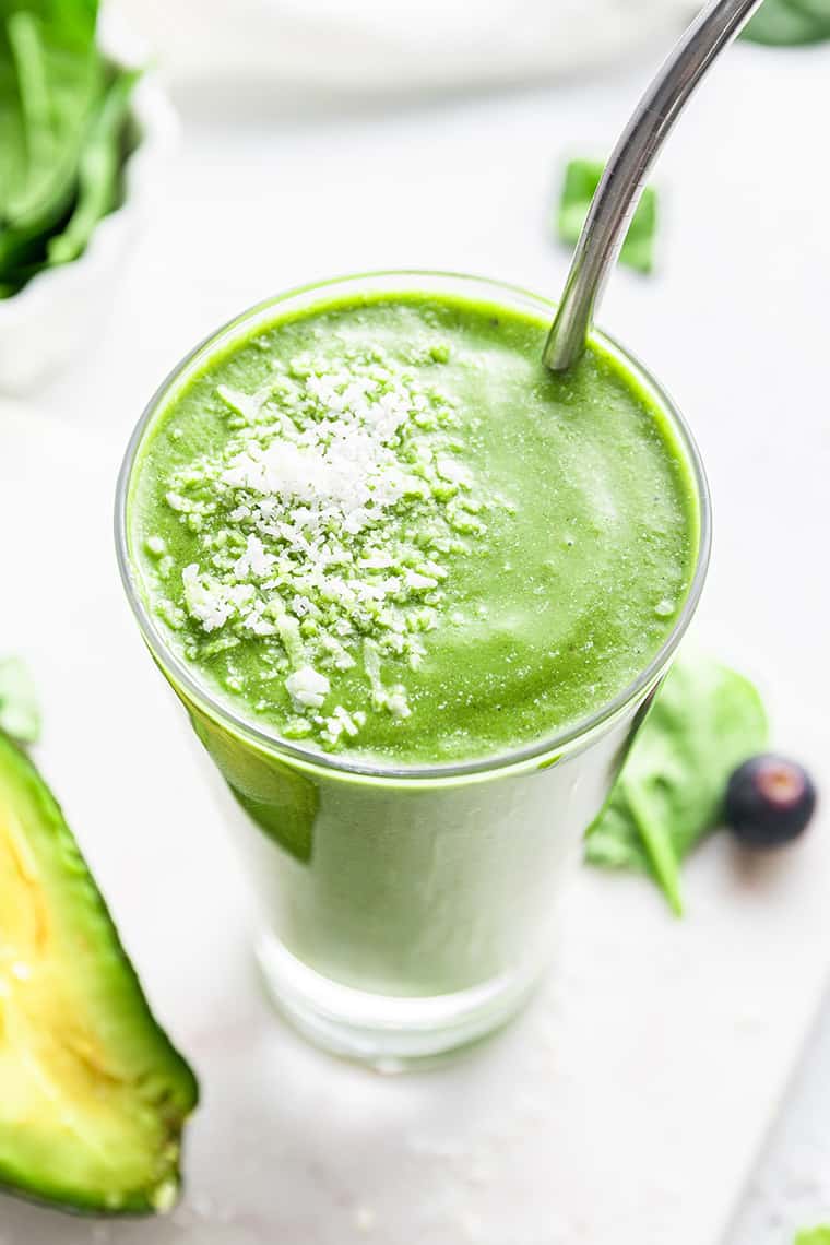 Green smoothie in tall glass with stainless steel straw and shredded coconut garnish