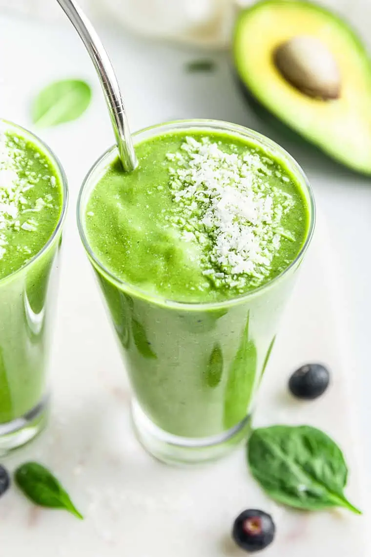 Angled top-down view of green smoothie in glass with stainless steel straw and shredded coconut garnish