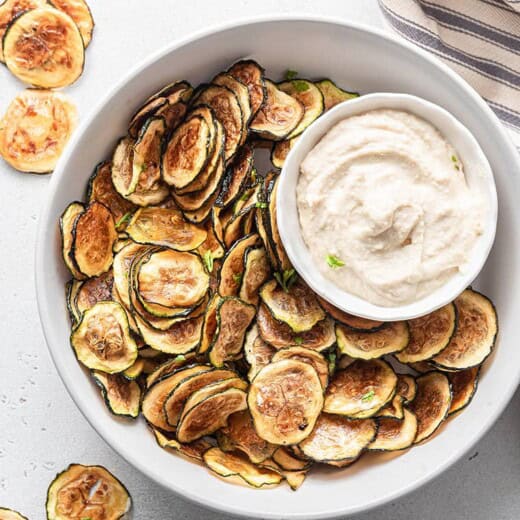 Overhead view of zucchini chips in large bowl with bowl of dip