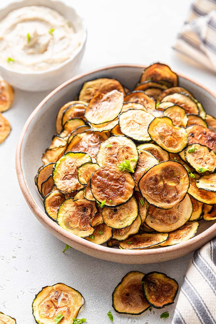 Large bowl of homemade zucchini chips with bowl of dip in background