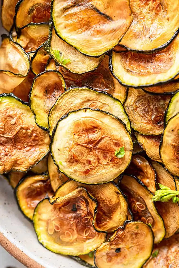 Zucchini chips piled into bowl, garnished with herbs