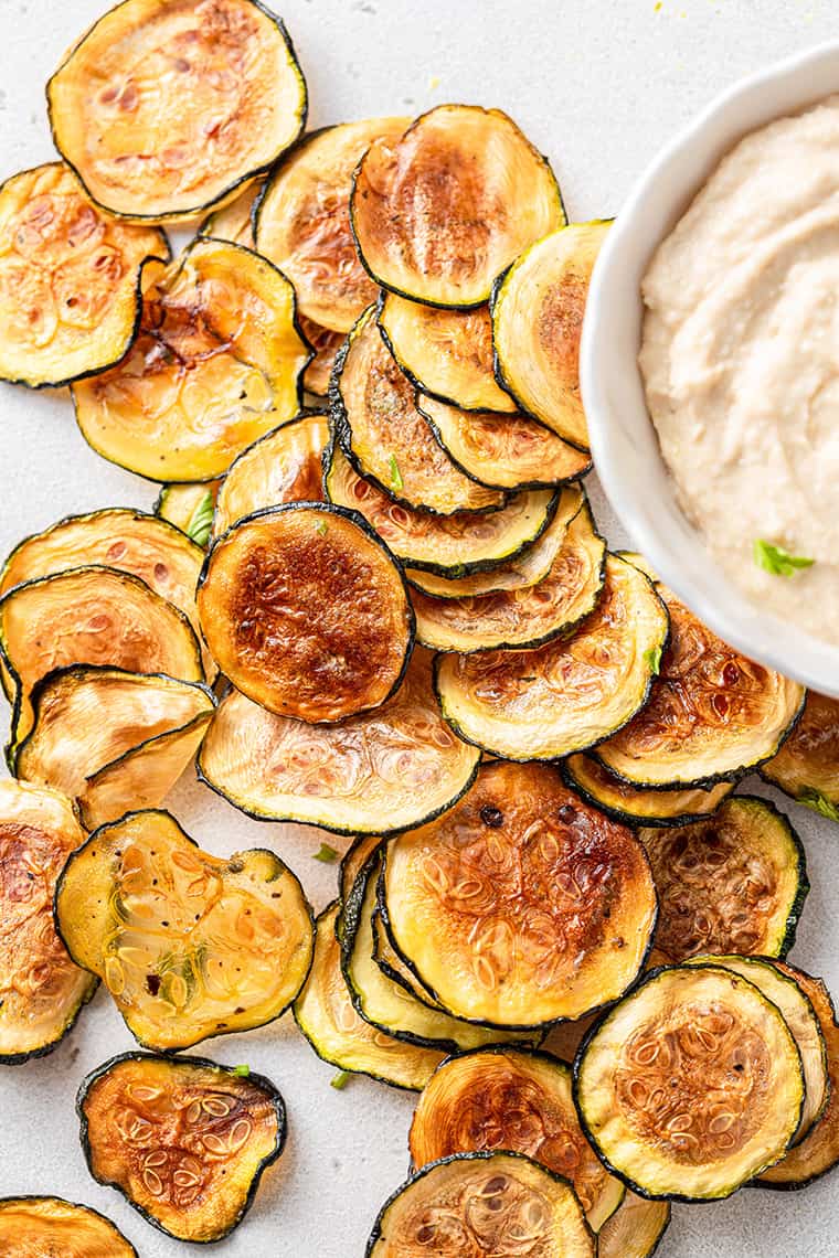 Crispy zucchini chips piled next to bowl of dip