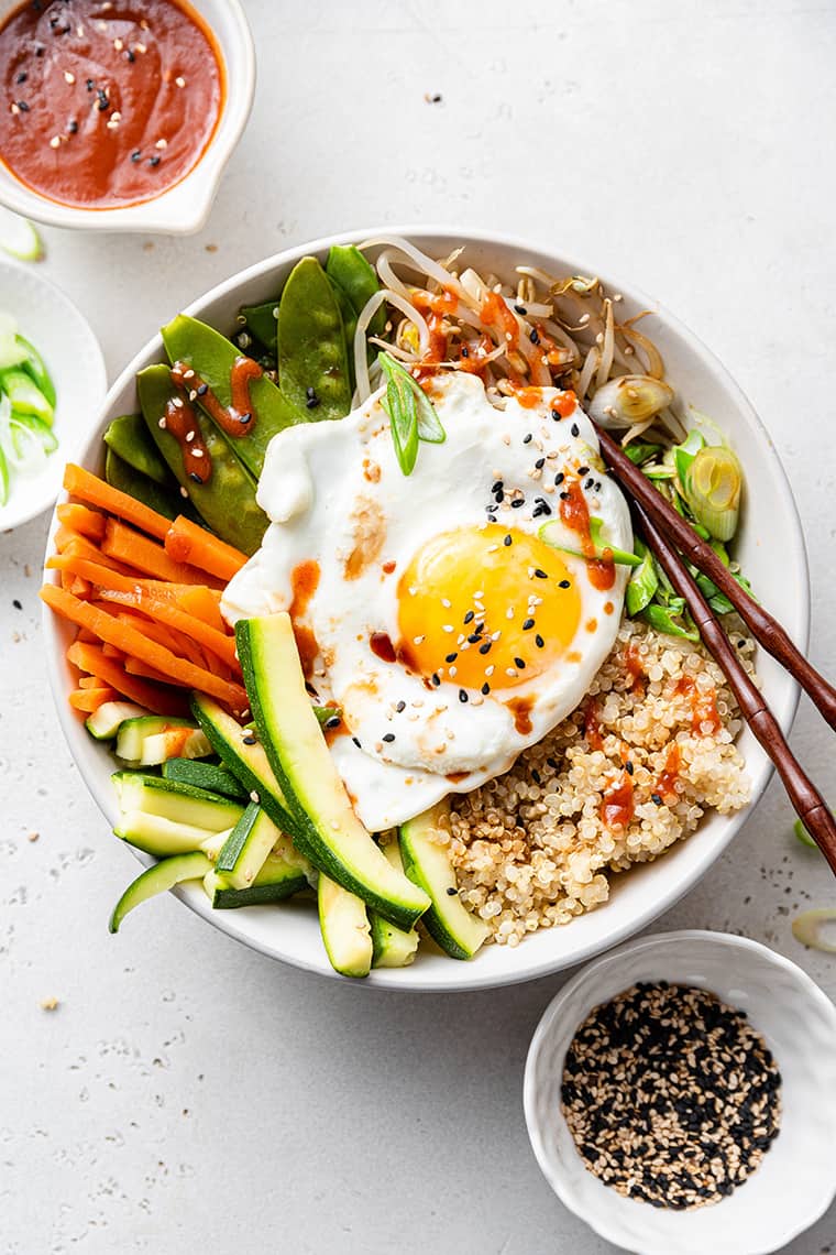 Overhead view of quinoa bibimbap bowl with steamed veggies and sunny side up egg