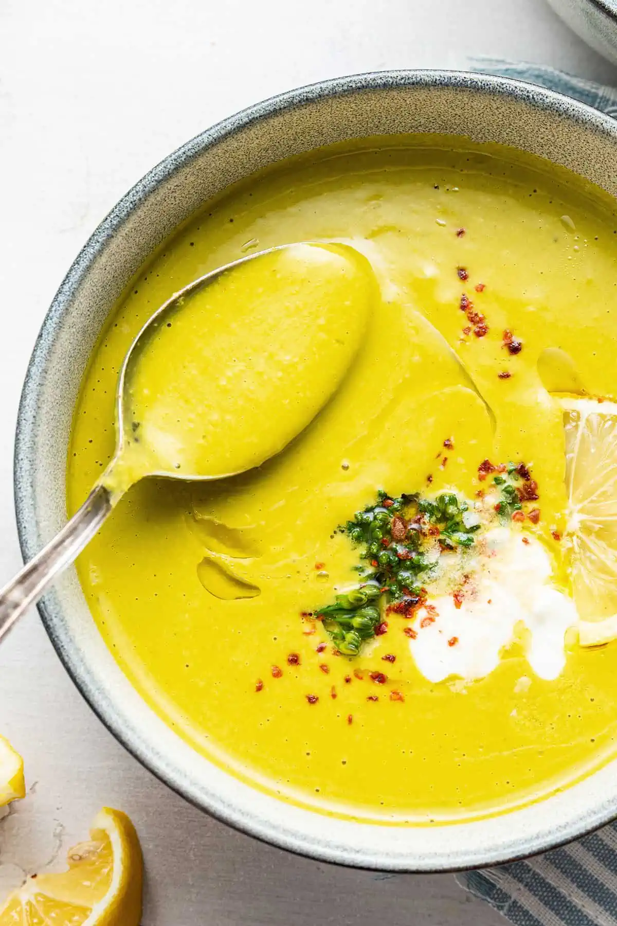 Close up overhead view of a bowl of broccoli soup topped with broccoli, chili flakes, and vegan creme fraiche, with a spoon taking a spoonful out