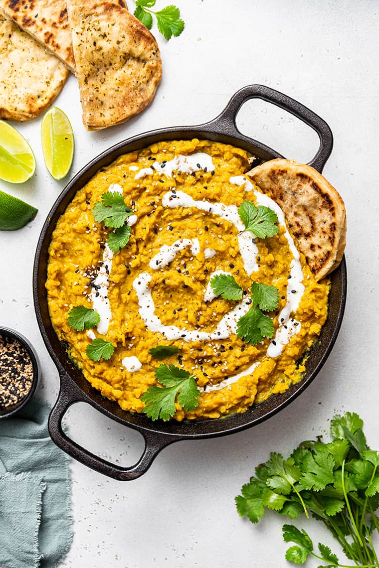 Overhead view of red lentil dal in black serving bowl with handles, garnished with coconut milk, cilantro, and spices