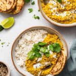 Overhead view of red lentil dal in two bowls, one with white rice and flatbread