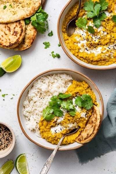 Overhead view of red lentil dal in two bowls, one with white rice and flatbread