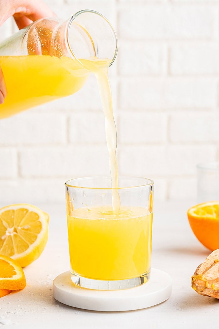 pouring a lemony adrenal drink into a glass with a pitcher