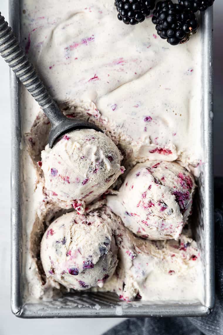 Three scoops of black raspberry ice cream set atop pan of ice cream
