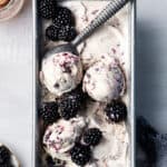 Overhead view of black raspberry ice cream in loaf pan with ice cream scooper and fresh berries