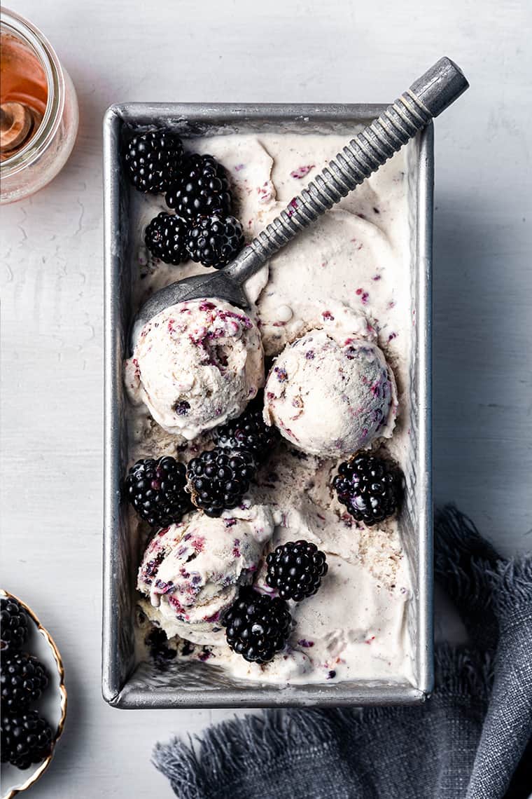 Overhead view of black raspberry ice cream in loaf pan with ice cream scooper and fresh berries