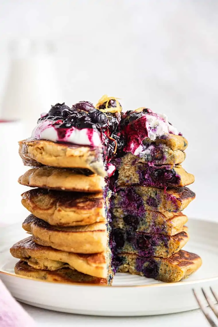 Tall stack of fluffy gluten-free pancakes on plate with yogurt, blueberry sauce and lemon zest