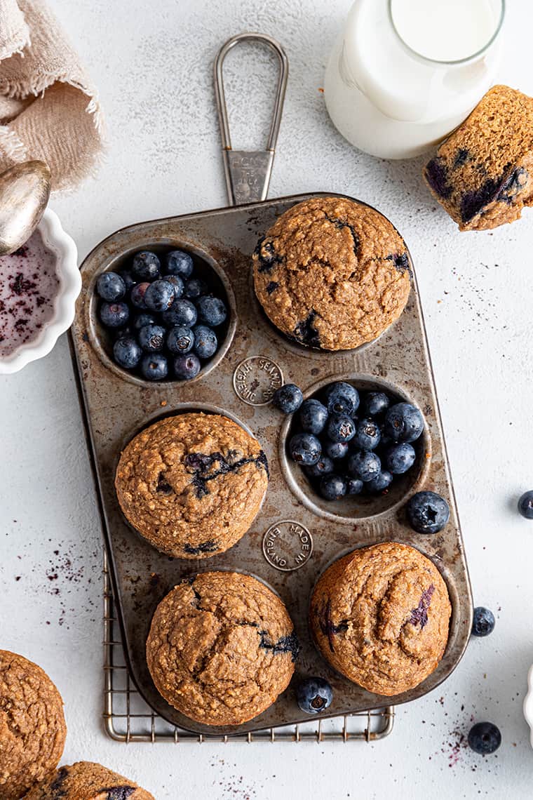 Rustic muffin tin with 4 cups filled with healthy blueberry muffins and 2 cups filled with blueberries