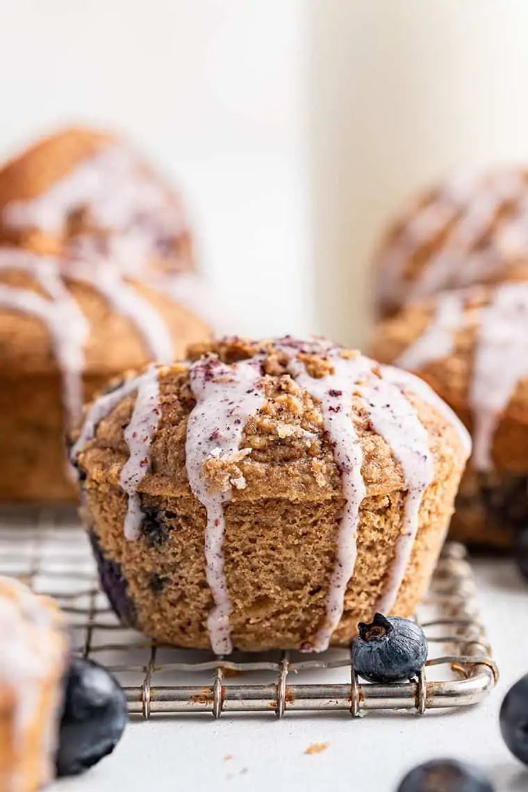 These easy blueberry oat muffins are tender, sweet, and delicious! Glazed blueberry muffin on cooling rack
