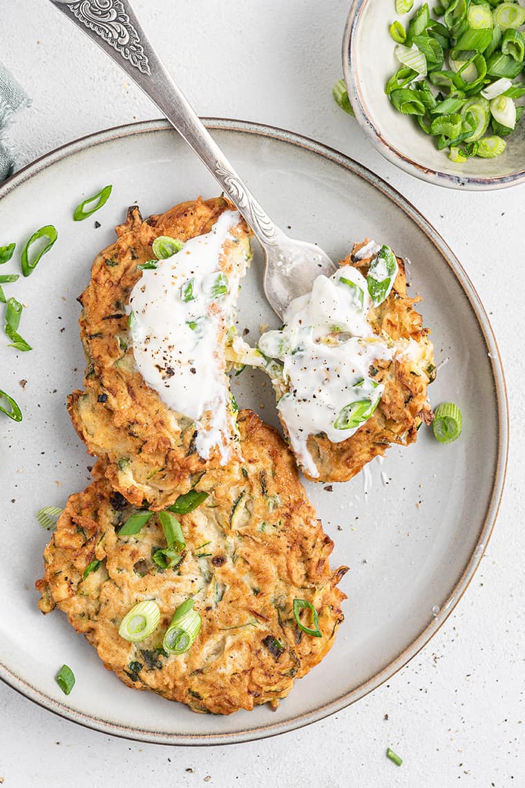 Overhead view of zucchini fritters on plate, topped with yogurt and scallions