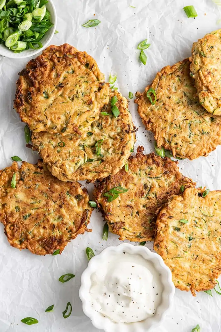Zucchini fritters on parchment paper with small bowls of dipping sauce and scallions