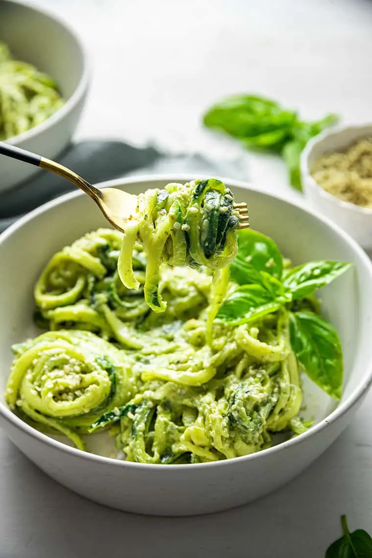 A bowl full of avocado pesto zucchini noodles with a fork lifting up one bite