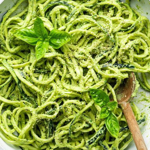 Creamy pesto zucchini noodles being stirred with a wooden spoon