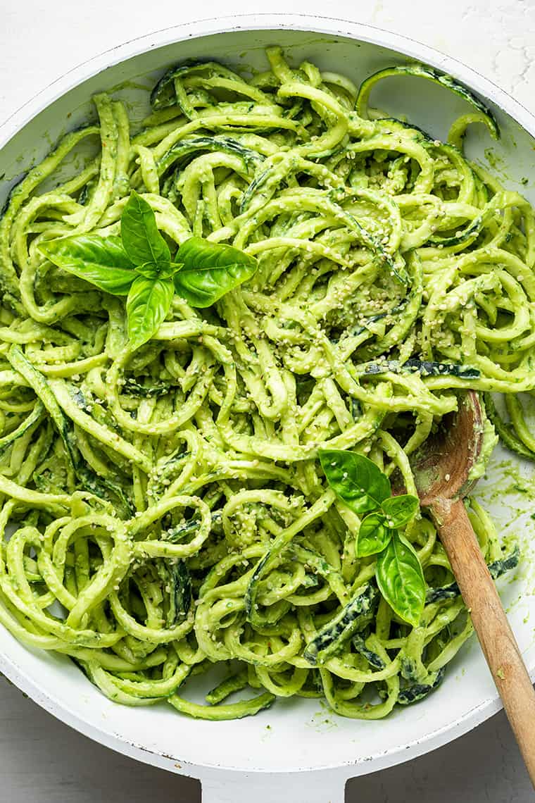 Creamy pesto zucchini noodles being stirred with a wooden spoon