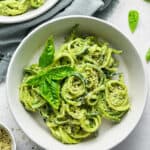 A serving of pesto zoodles in a shallow bowl with a second serving beside it