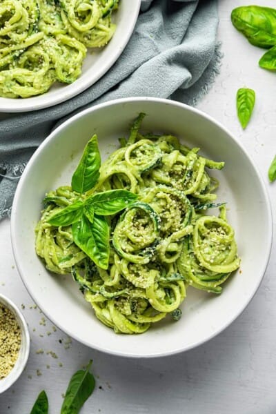 A serving of pesto zoodles in a shallow bowl with a second serving beside it