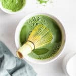 Bamboo whisk mixing matcha in white ceramic bowl