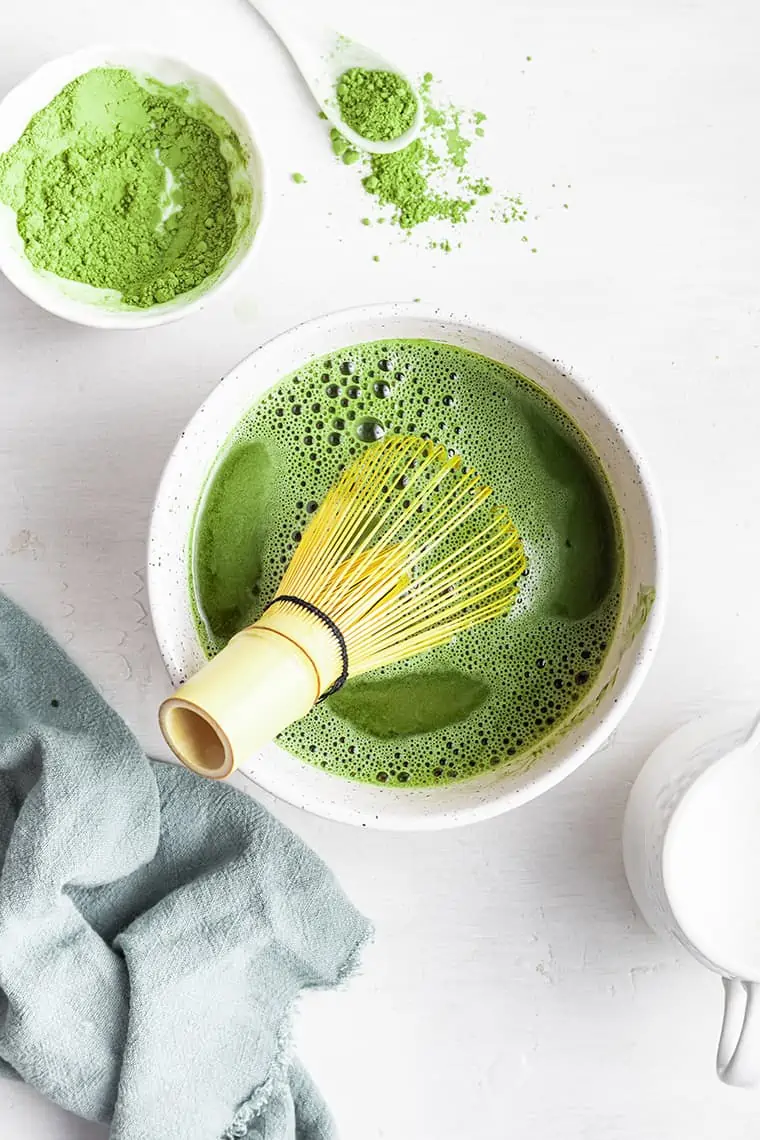 Bamboo whisk mixing matcha in white ceramic bowl