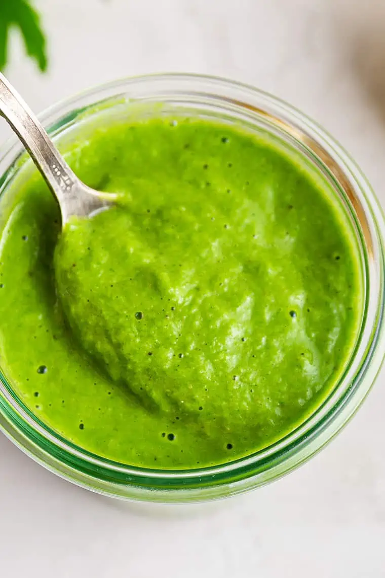 Overhead view of spoon in jar of healthy green goddess salad dressing
