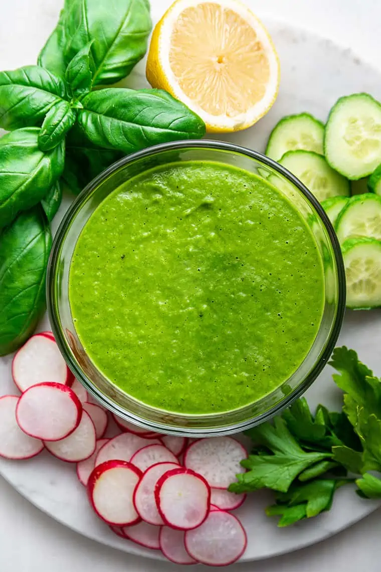 Overhead view of vegan green goddess salad dressing in bowl surrounded by crudites and herbs