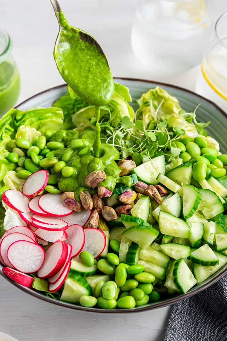 Drizzling spoonful of dressing onto green goddess salad