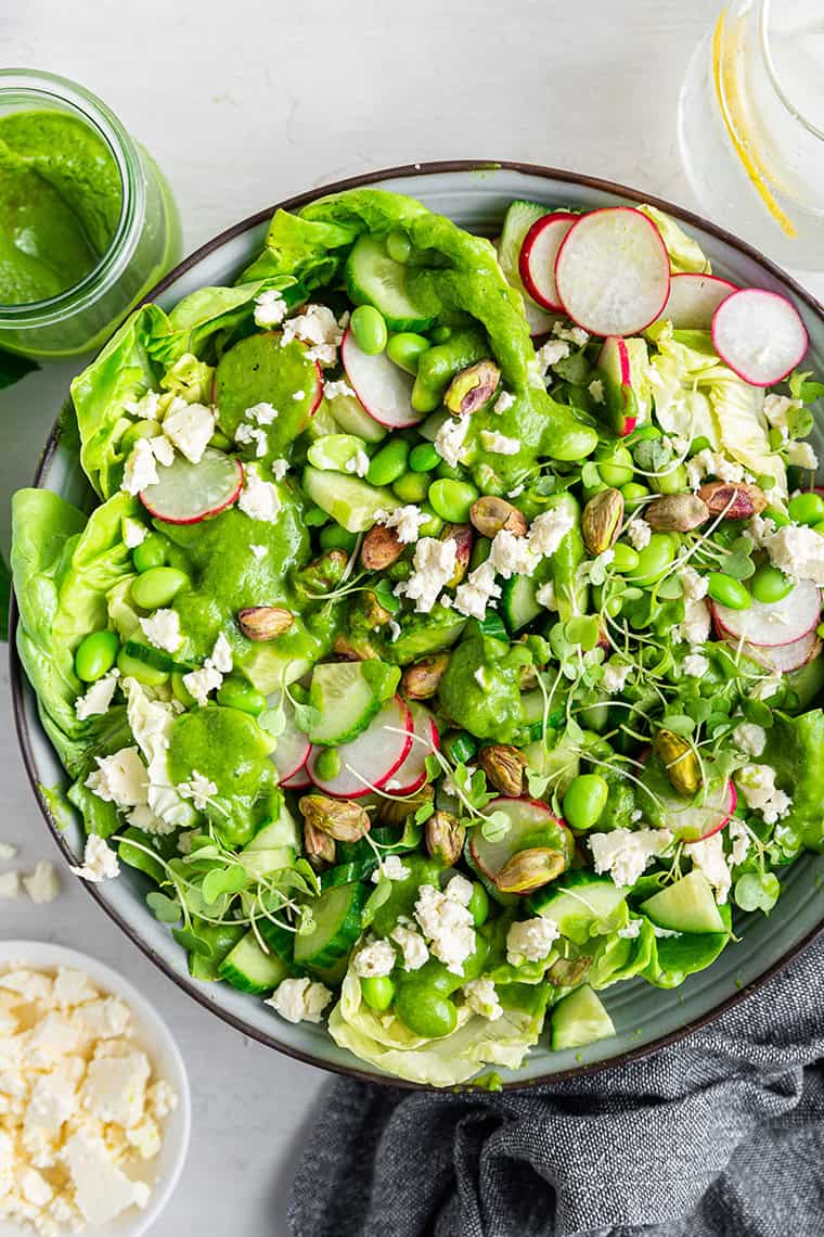 Green goddess salad in serving bowl with dressing and feta