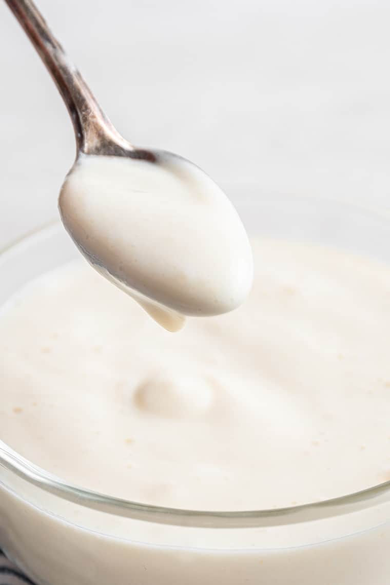 Spoon of vegan sour cream being held over bowl