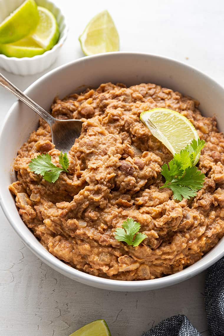 Bowl of vegetarian refried beans with cilantro and lime wedge