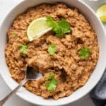 Vegetarian refried beans in white bowl with cilantro and lime wedge