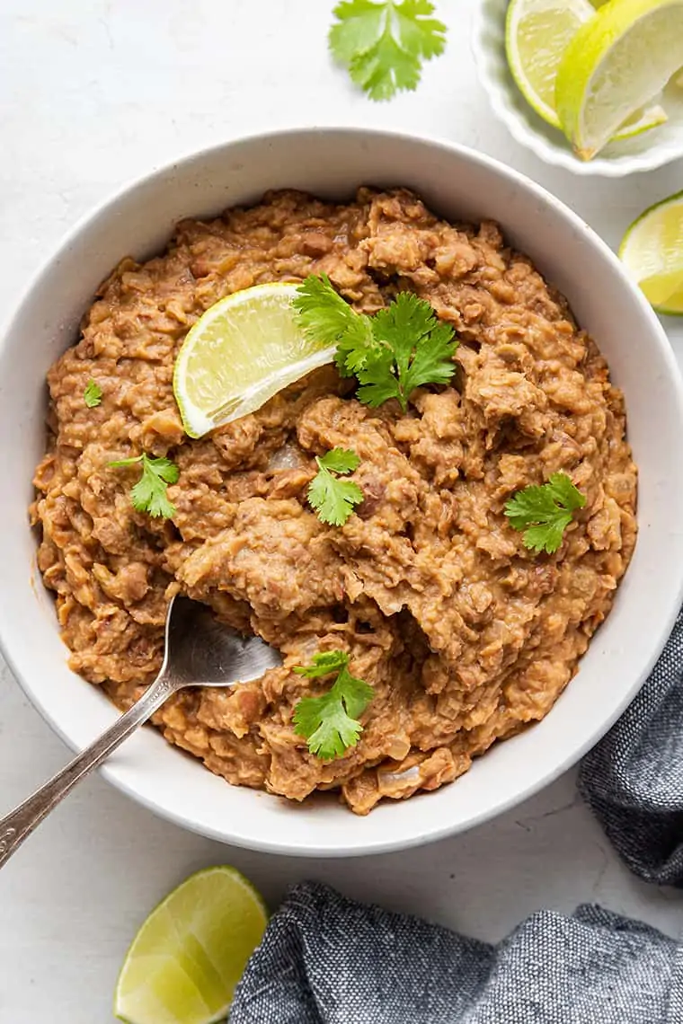 Vegetarian refried beans in white bowl with cilantro and lime wedge