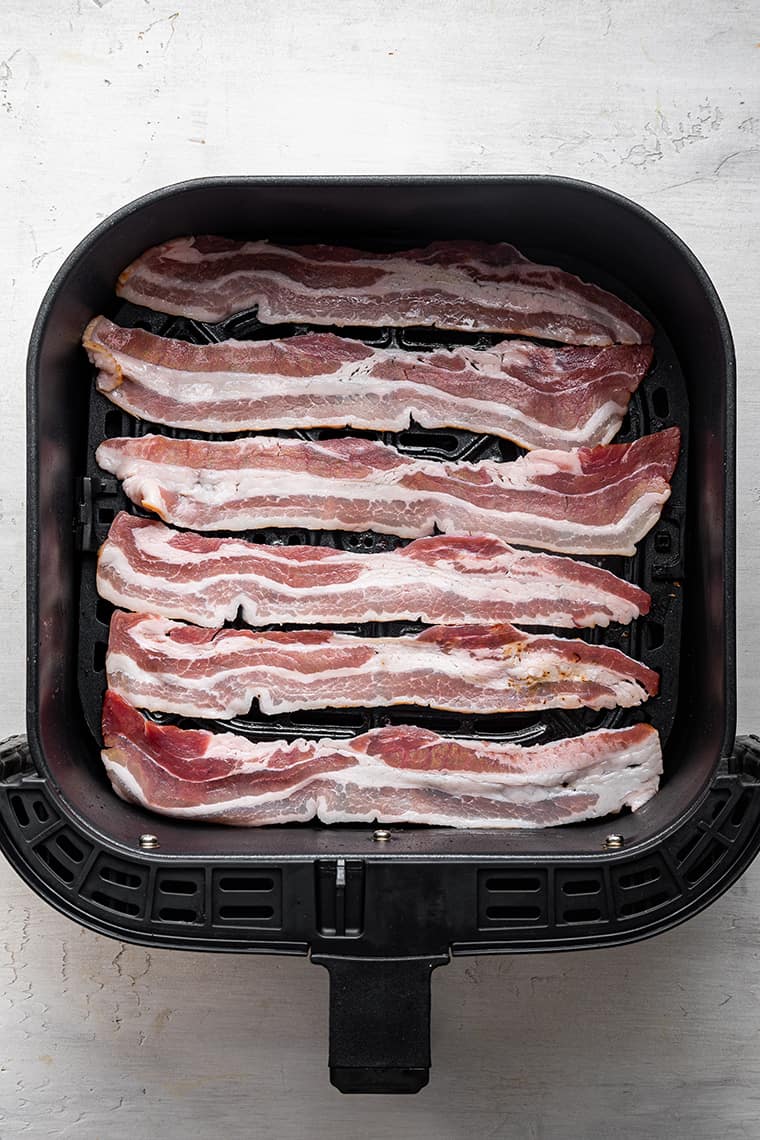 Horizontal slices of uncooked bacon in an air fryer basket