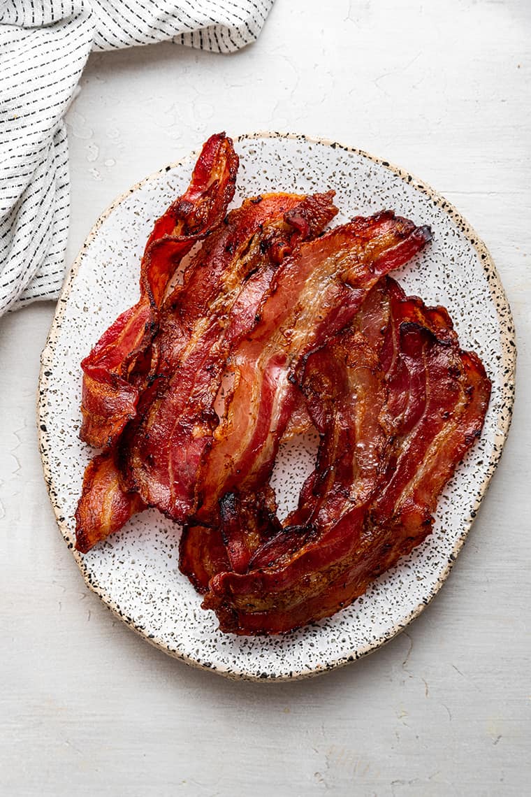 A white oval plate with a pile of cooked bacon on it