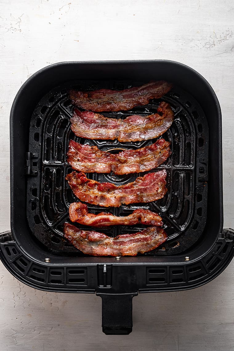 Horizontal strips of cooked bacon in an air fryer basket