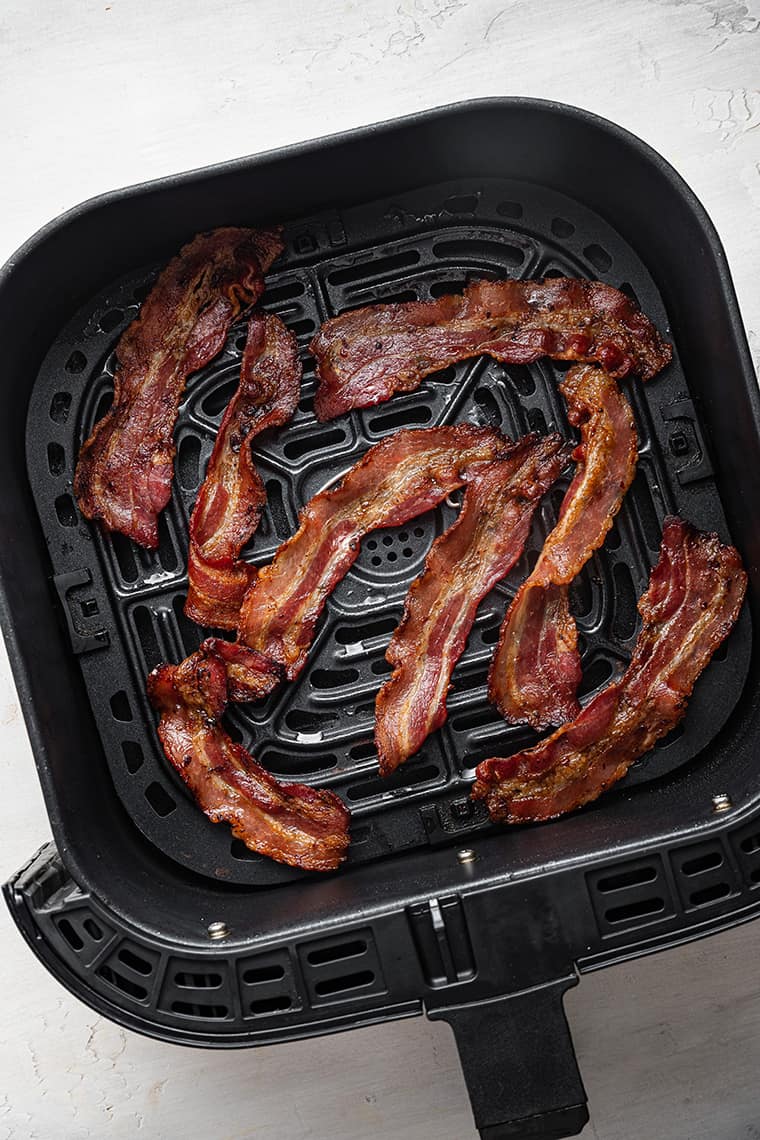 Randomly placed strips of cooked bacon in an air fryer basket