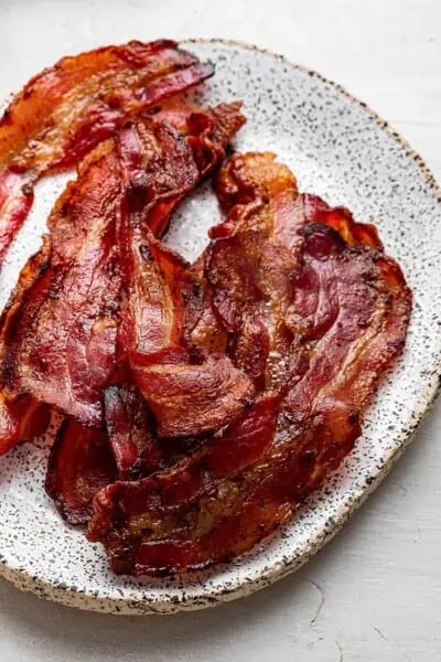 Close up of a pile of cooked and curled bacon on a speckled plate