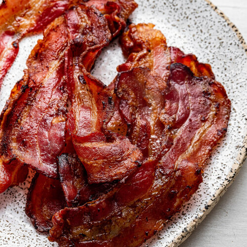 Close up of a pile of cooked and curled bacon on a speckled plate