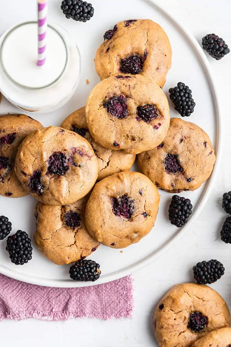 If you like your cookies soft and chewy, you’ll love this healthy Blackberry Cookie recipe. Gluten-free, dairy-free, and refined-sugar-free! Overhead view of blackberry cookies on platter with glass of milk