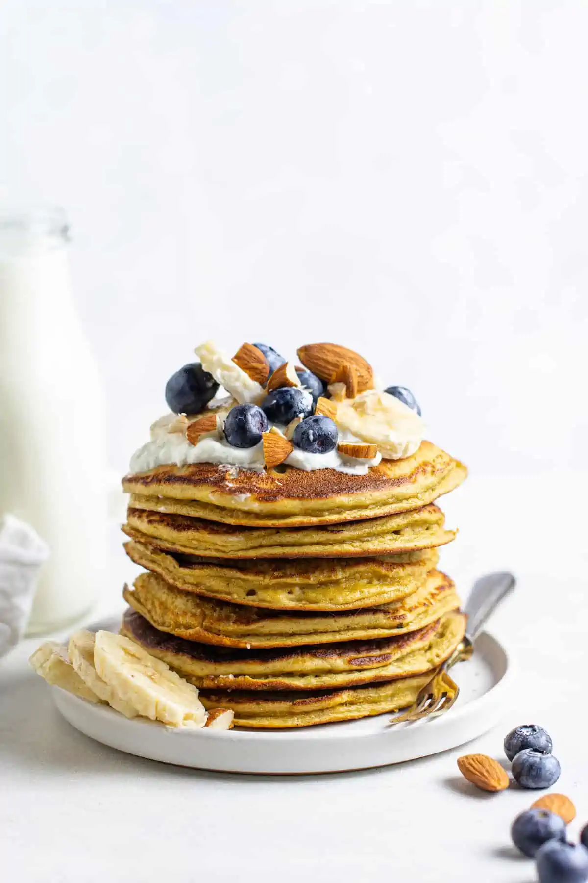 These protein pancakes are fluffy and flavorful, made with 6 ingredients in the blender. Gluten-free, dairy-free, and meal prep-friendly! A stack of protein pancakes on a plate topped with fresh fruit and nuts.